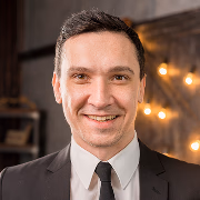 Smiling middle-aged man in a dark professional suit and white shirt, featuring a warm and approachable expression.