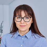 Portrait of a woman with long brown hair and bangs wearing glasses and a light blue button-down shirt.