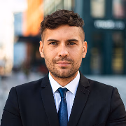 Professional portrait of a young man with a beard and short dark hair, wearing a dark blue suit and a blue necktie.